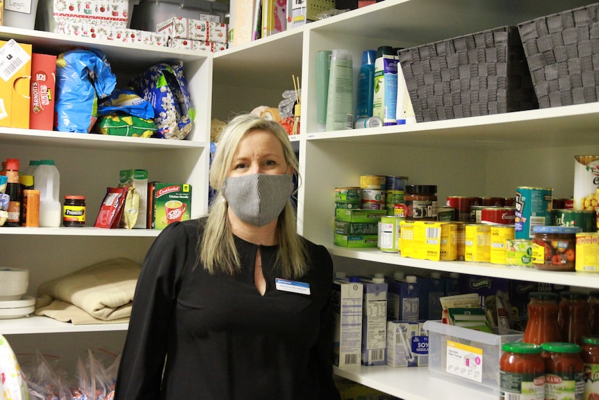 A woman wearing a face mask stands in front of shelves of food.