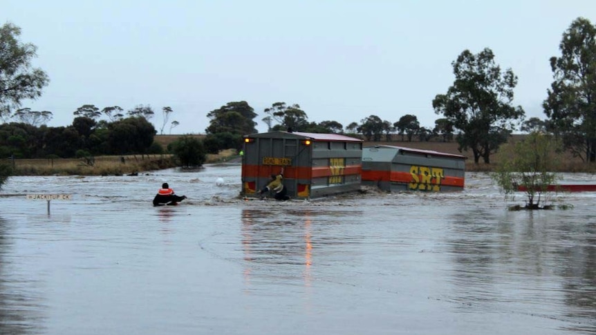 A truck driver is thrown a rope as he hangs off the back of his road train, which is partially submerged by floodwaters.