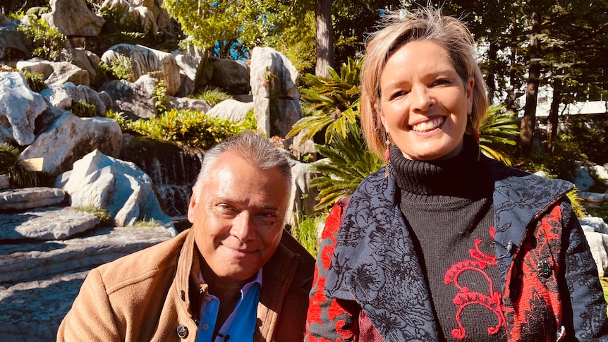 Man and woman smiling to camera with garden in background.