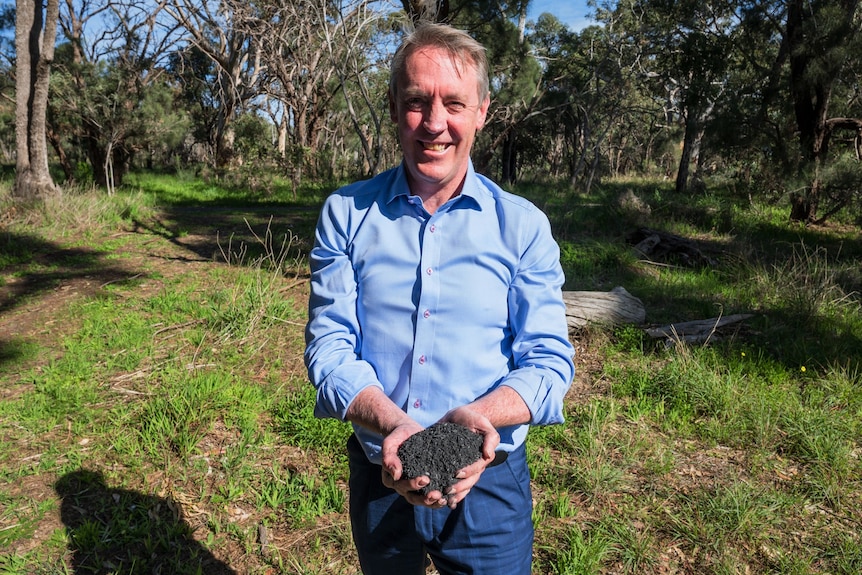 A man holds a handful of black biochar.