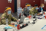 Four people sitting at a desk wearing personal protective equipment 