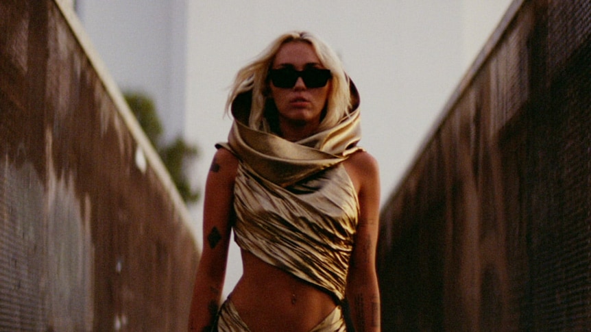 Miley Cyrus wearing a gold dress and sunglasses