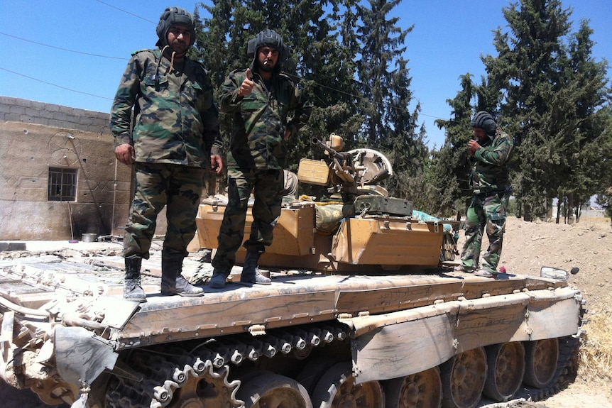 Syrian soldiers stand on a tank near Damascus