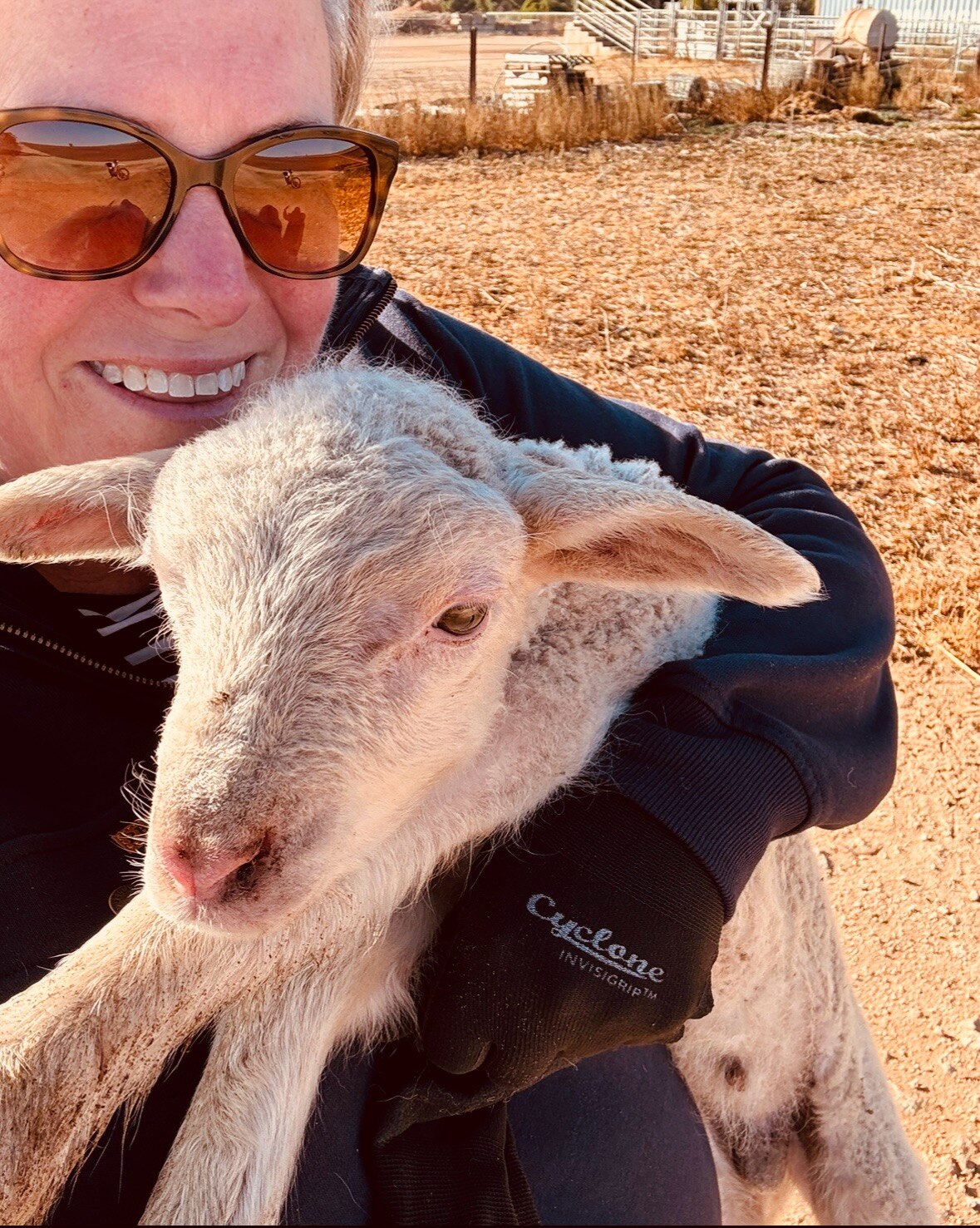 Foto selfie de la esposa de un granjero con gafas de sol y un cordero joven en la mano