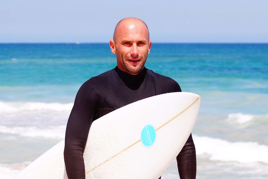 Damon Hayes in a wetsuit with his surfboard at Trigg Beach