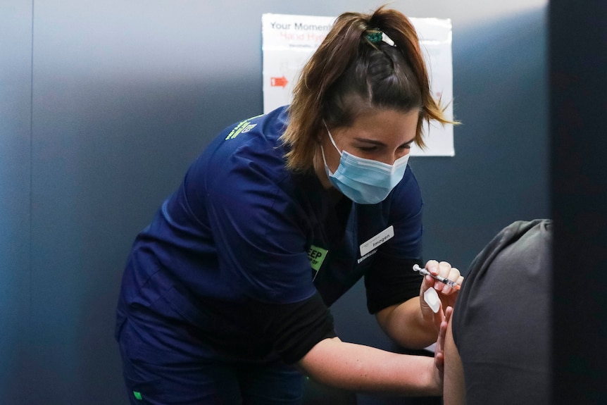 Masked nurse gives Pfizer vaccine to patient at COVID-19 clinic.