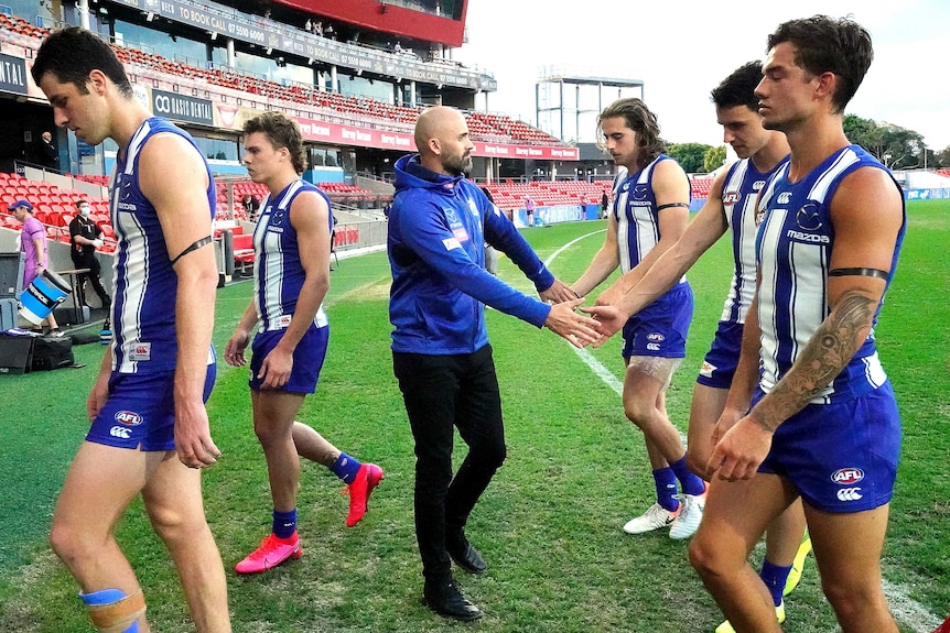 Five North Melbourne AFL players walk off the ground, as one shakes hands with their coach on the Gold Coast.