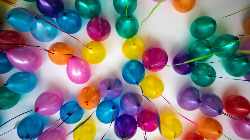 Colourful helium balloons with streamers attached floating under a ceiling