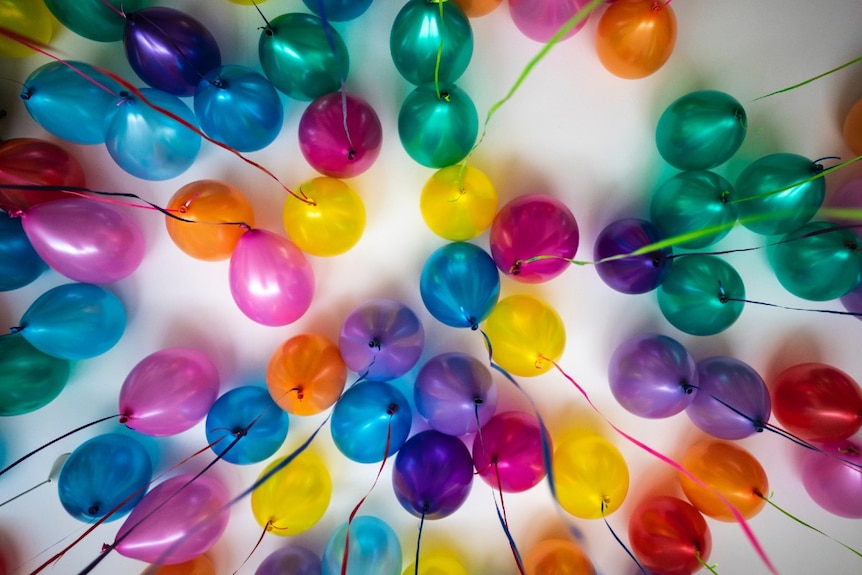 Colourful helium balloons with streamers attached floating under a ceiling.
