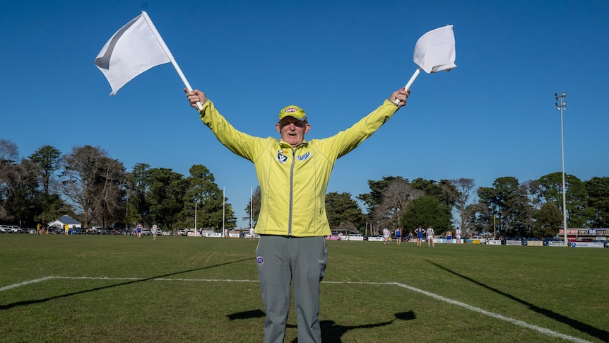 a man waves the white umpire flags on a footy field.
