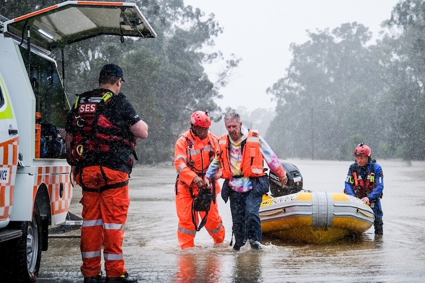 A man being helped out of floodwater, a boat in background