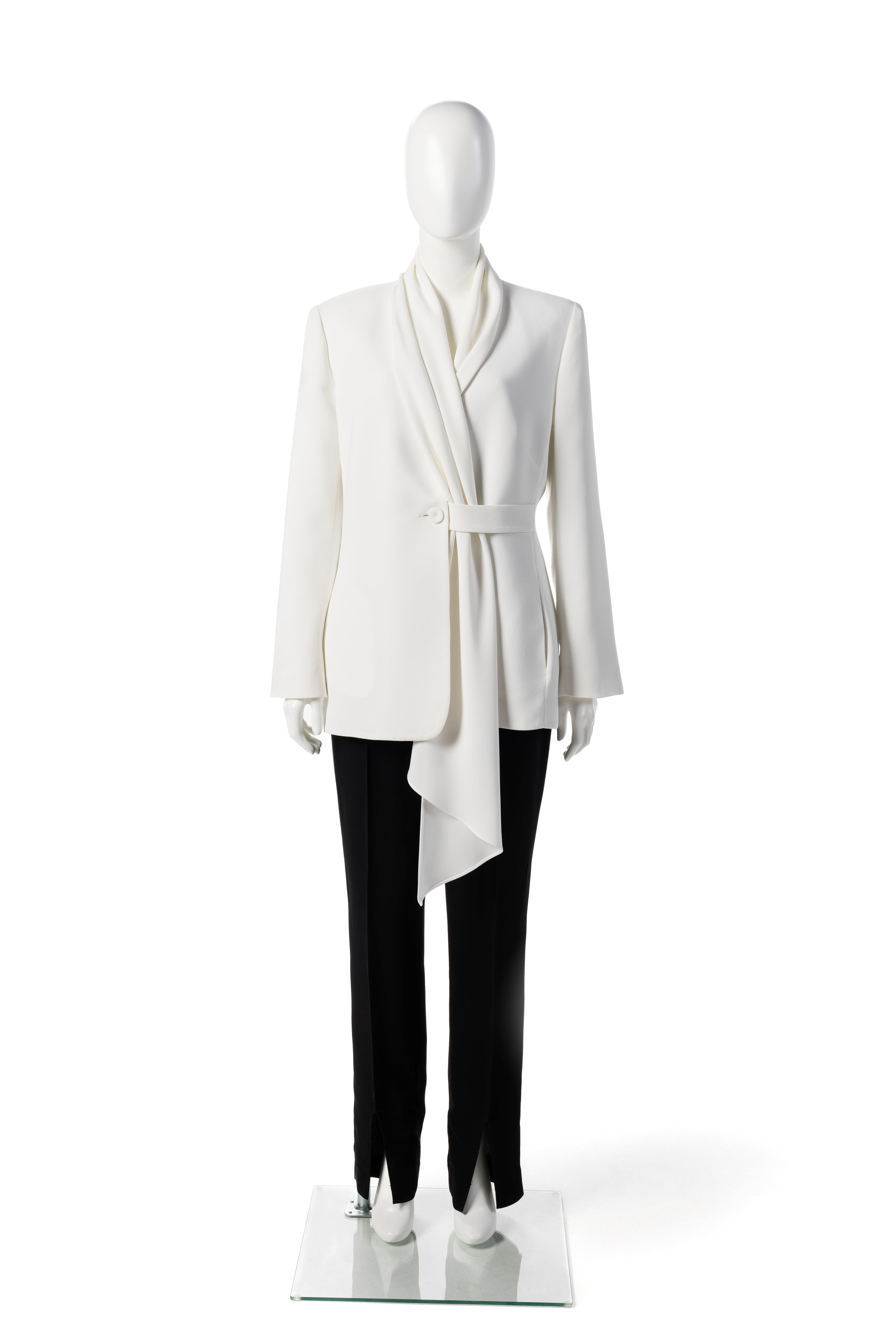 A white mannequin wears a white blazer with a shawl-like tie detail at the front and slim black pants.