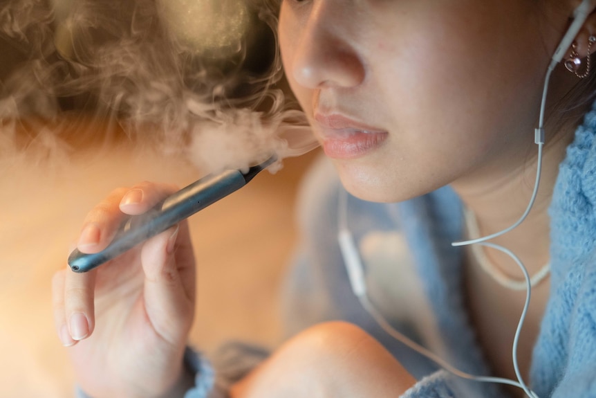 Young woman vaping an electronic cigarette, with headphones plugged in.