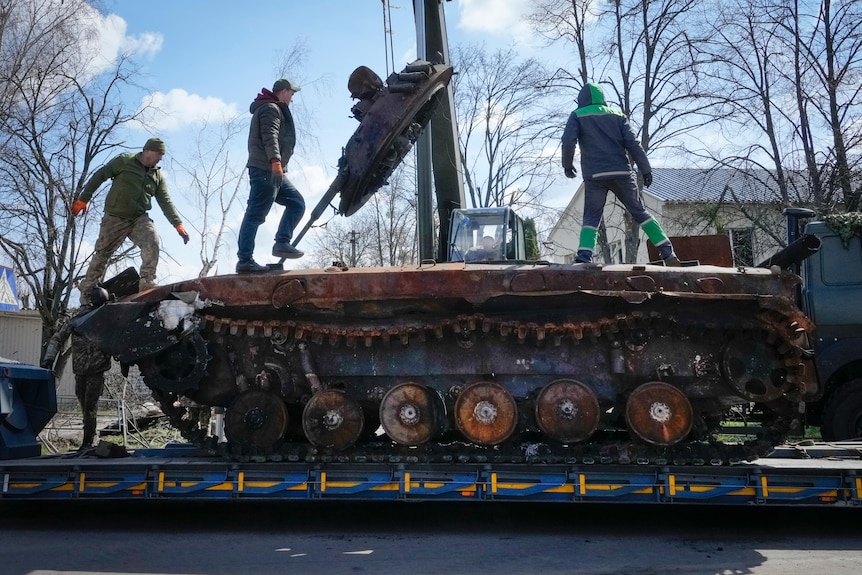 Three men stand on a military tank getting towed
