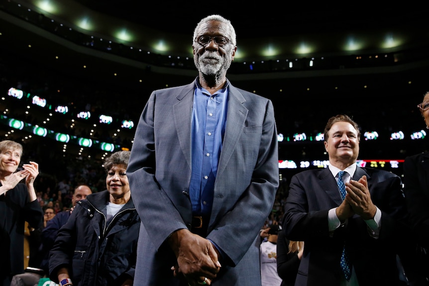 Bill Russell standing in a gray suit at an NBA game