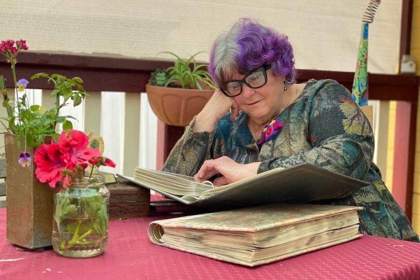 Lady with purple hair looks through albums.