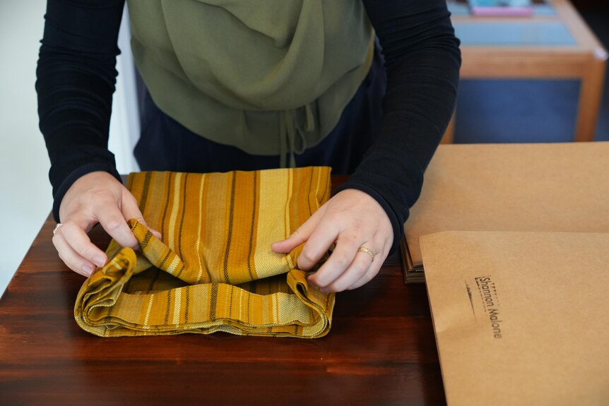 A woman folding a piece of orange striped fabric.
