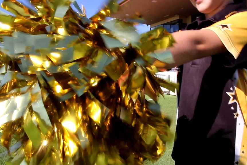 A close up image of a cheerleader holding a gold pompom