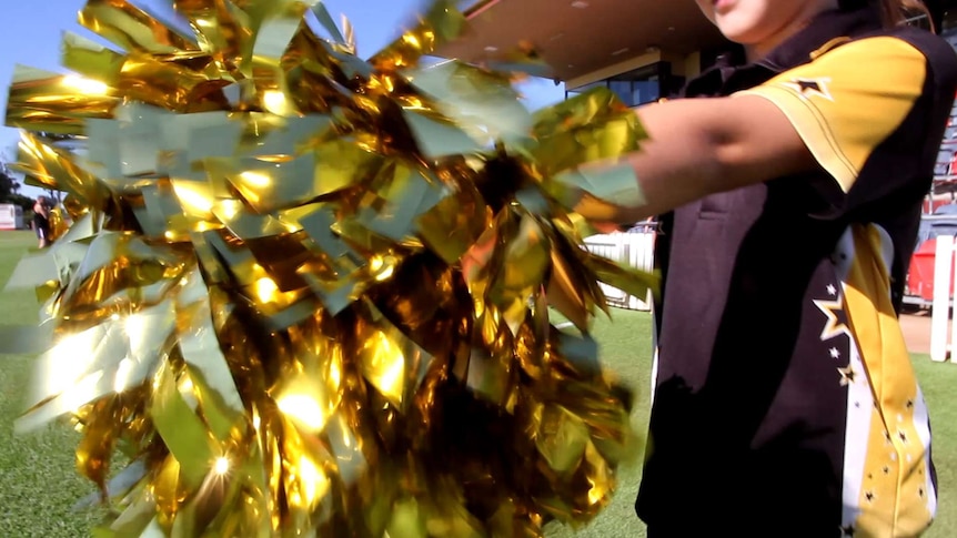 A close up image of a cheerleader holding a gold pompom