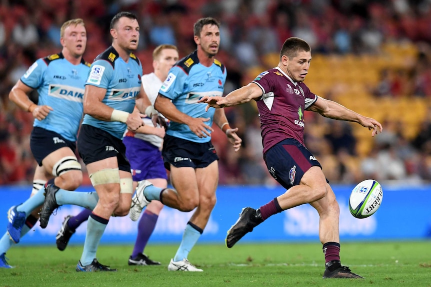 James O'Connor kicks the ball as three players wearing blue watch on