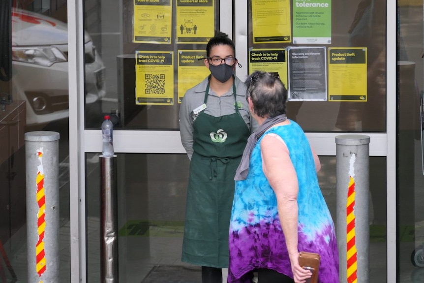 The exterior of a supermarket with a worker talking to an unidentifiable woman.