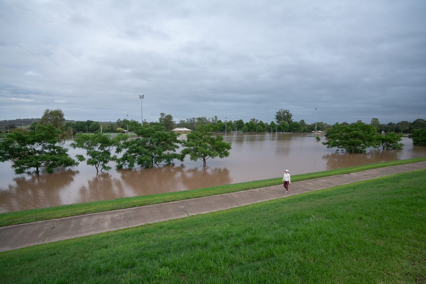 A woman walks down a concrete path next to a flooded sports ground.