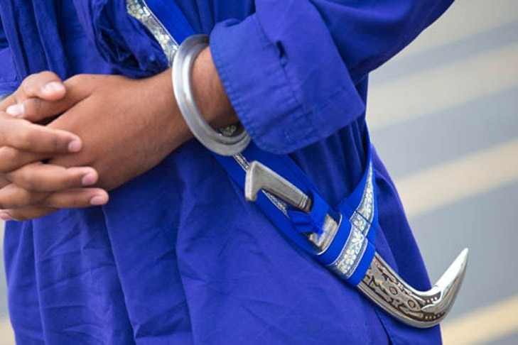 a close up of a curved dagger, known as a Kirpan, hanging from the belt of a robe