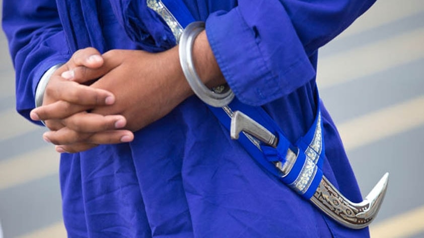 a close up of a curved dagger, known as a Kirpan, hanging from the belt of a robe