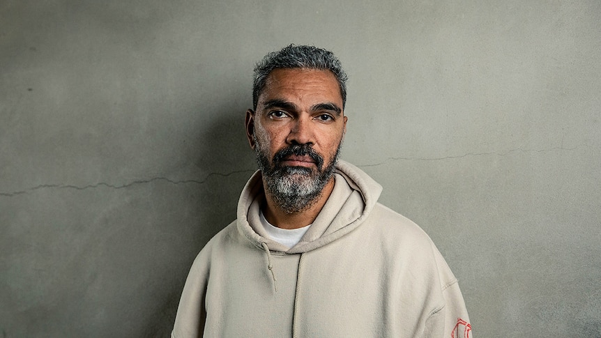 Colour photo of artist Daniel Boyd standing against concrete wall.