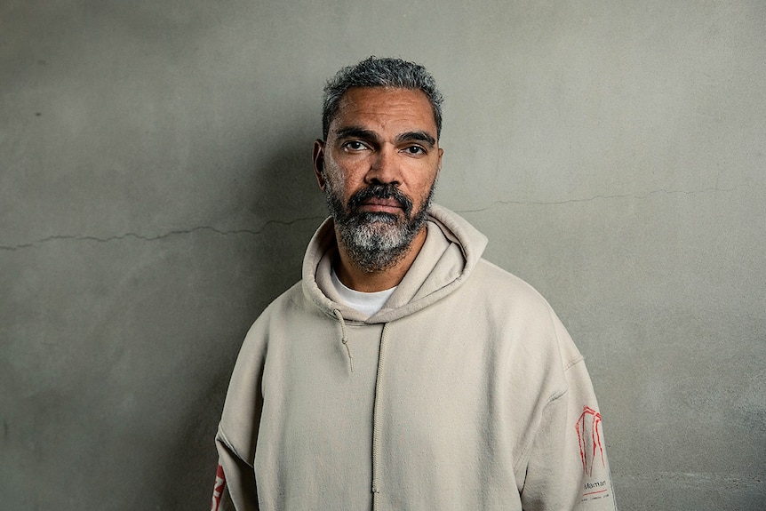 Colour photo of artist Daniel Boyd standing against concrete wall.