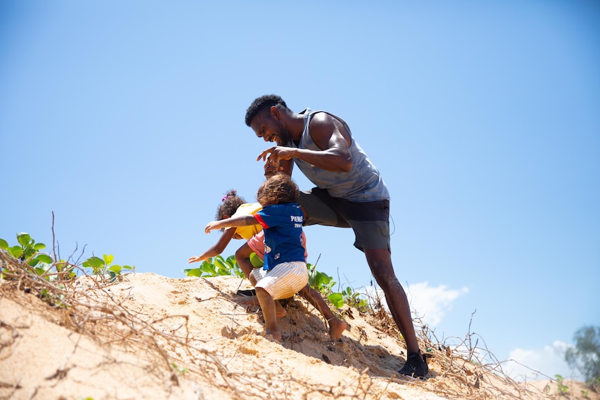 A man stands on a beach, playing with two infant girls