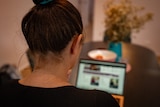 The back of a woman's head looking at a laptop screen on a table.