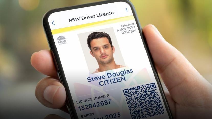 A person holds a mobile phone in their hand with the screen open to a digital licence with driver's photograph.
