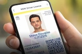 A person holds a mobile phone in their hand with the screen open to a digital licence with driver's photograph.