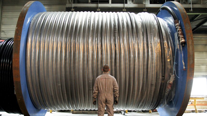 Man stands in front of a large drum of cable.
