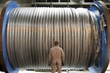 Man stands in front of a large drum of cable.