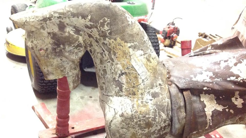 A rocking horse with no paint, no mane, missing part of its head, and badly neglected.