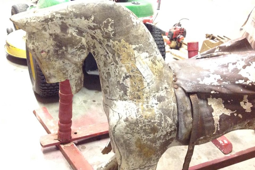 A rocking horse with no paint, no mane, missing part of its head, and badly neglected.