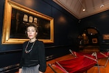 Curator Jessica Bridgfoot standing in front of the historical painting  Too late by Herbert Schmalz.