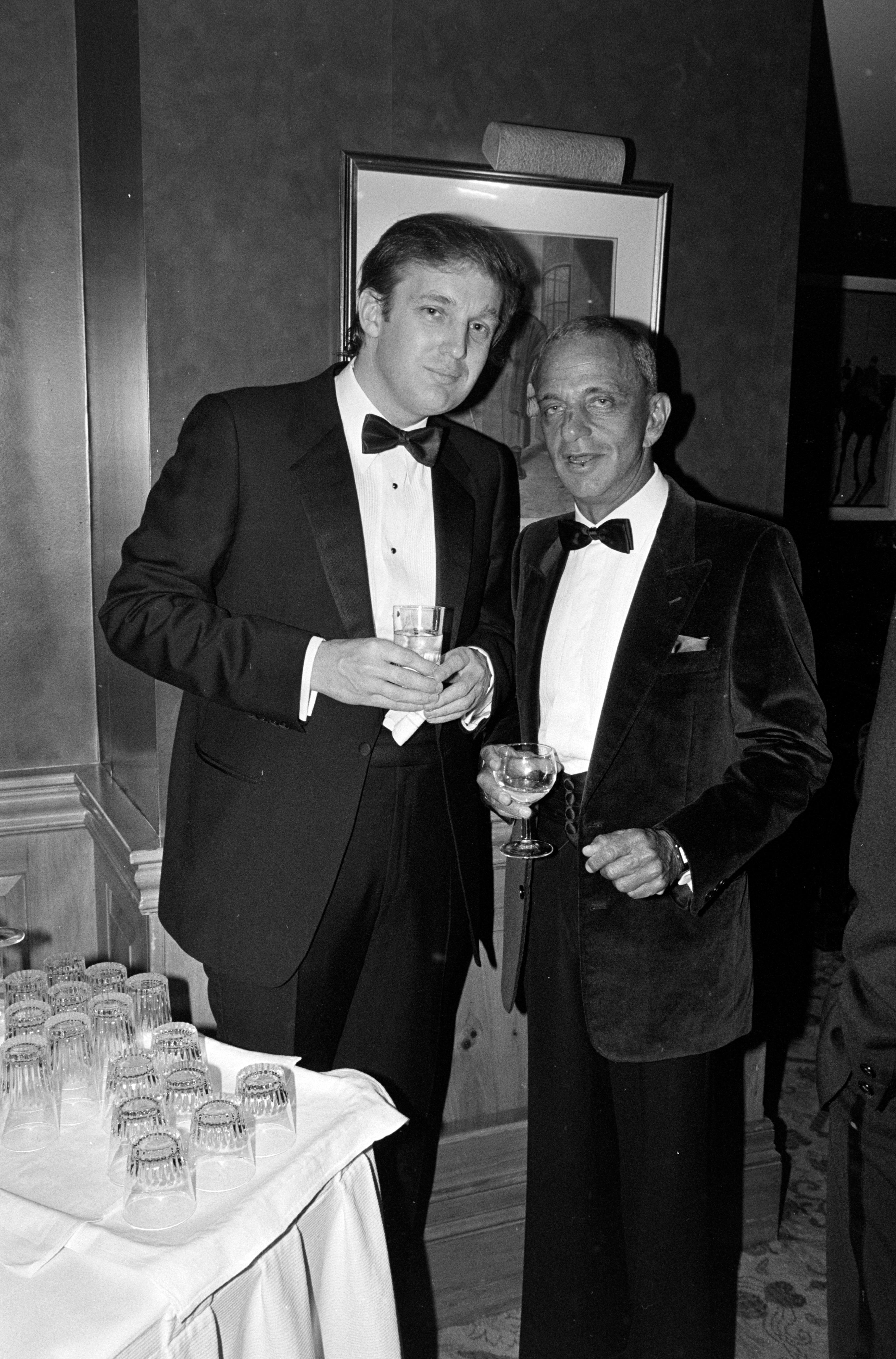 Two men dressed in suits stand near a table of glasses