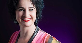 A woman with hoop earings and bright coloured top smiles widely.