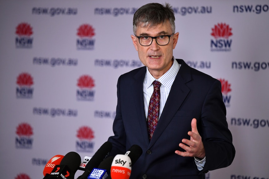 a man wearing glasses speaking and gesturing with his hands