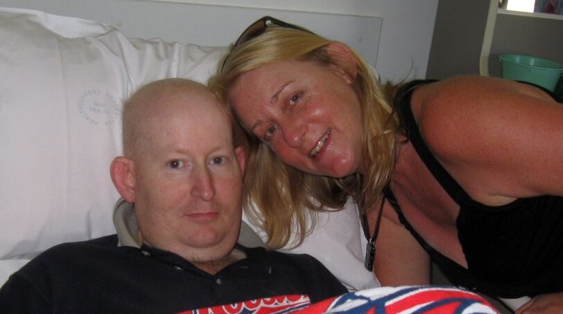 Colour image of bald man in hospital bed with a woman by his side