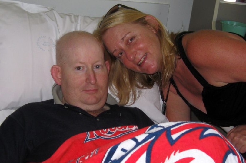 Colour image of bald man in hospital bed with a woman by his side