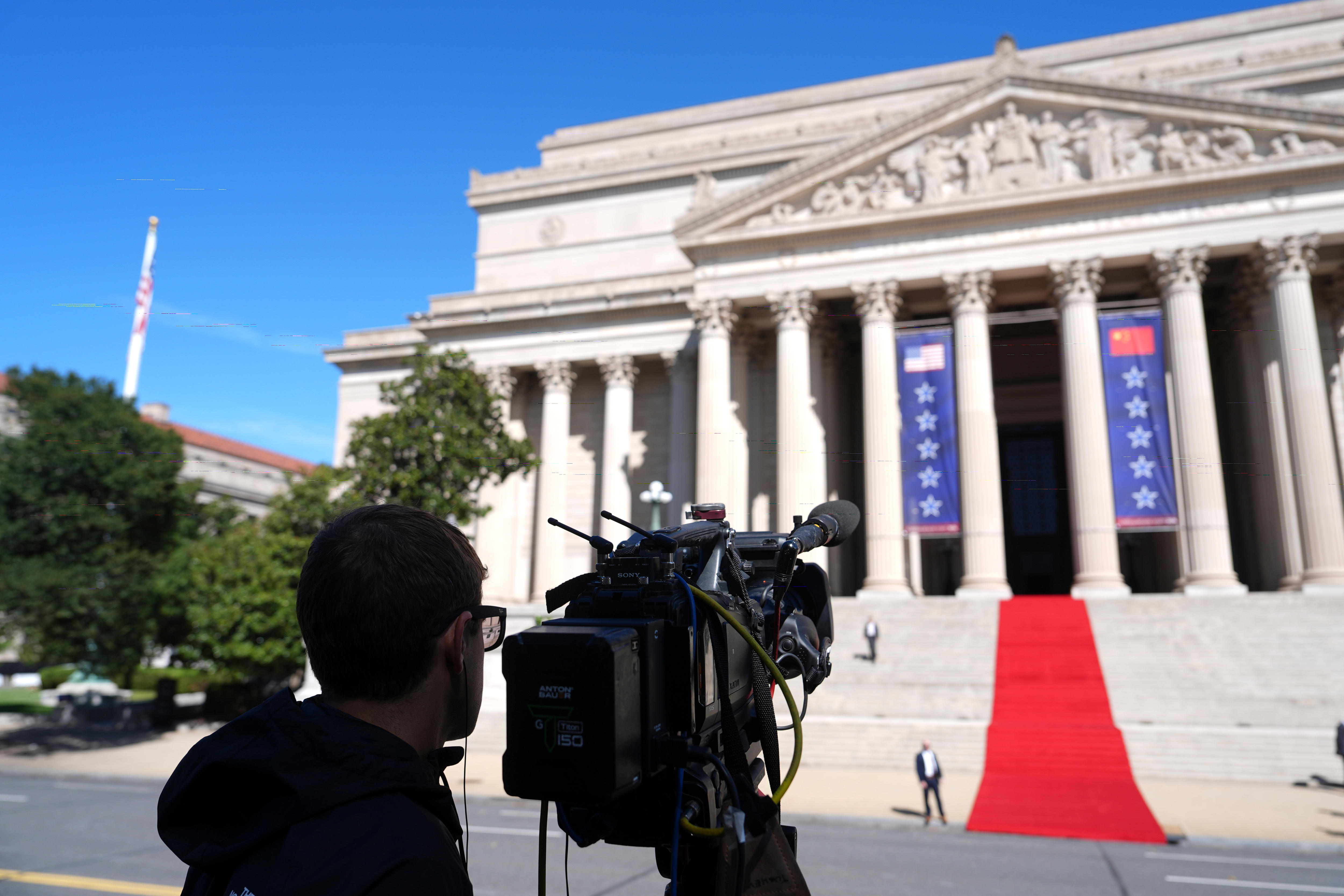 A camera operator set up in front of a large white building