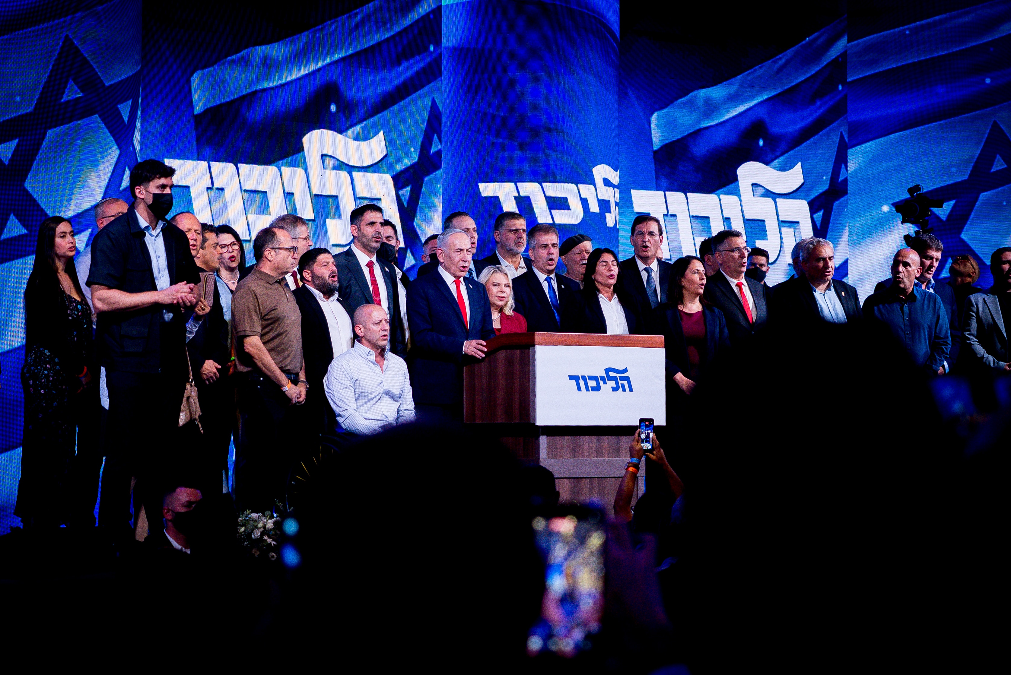 Netanyahu standing amongst a crowd on stage