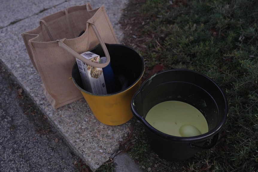 A bag and two buckets, one containing yellow paint. 