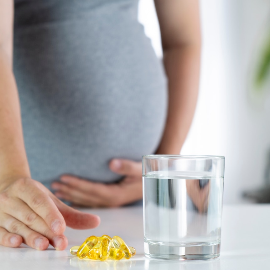 pregnant women with oil-filled gel capsules, and a glass of water