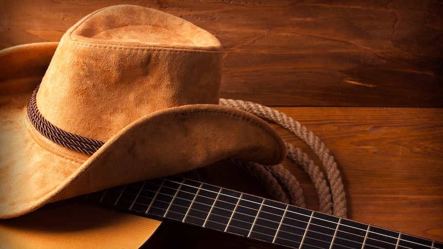 A farmer's felt hat sitting on top of a guitar.