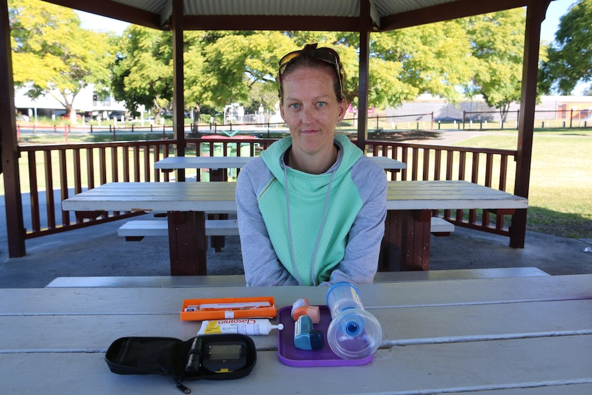 Woman sits at a table in a park shelter with medical equipment in front of her. 